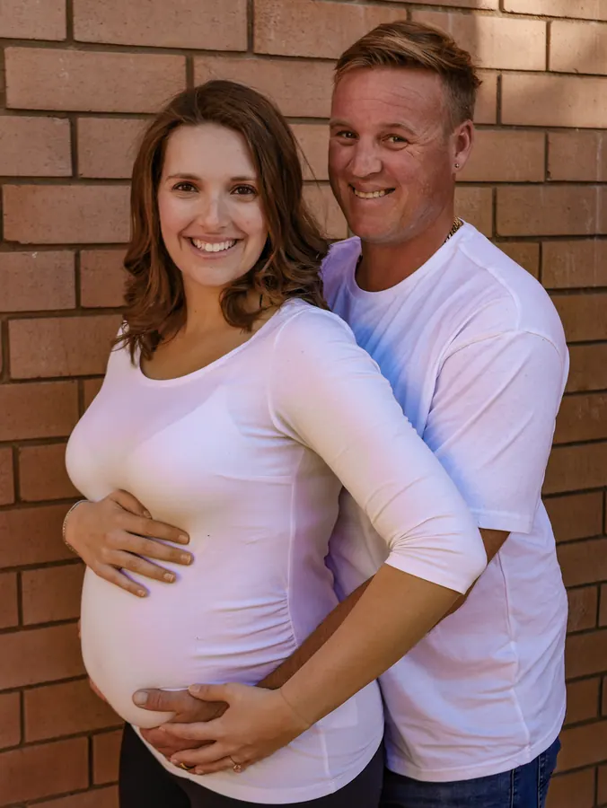 Courtney pregnant with her first baby, held by her husband against a brick wall