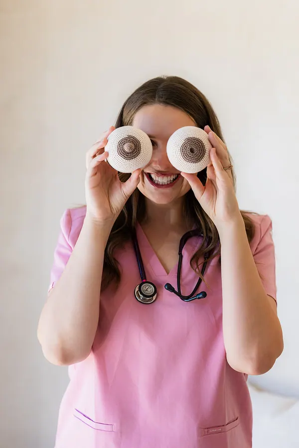 Courtney in her scrubs, laughing, holding two knitted breast models up to her eyes