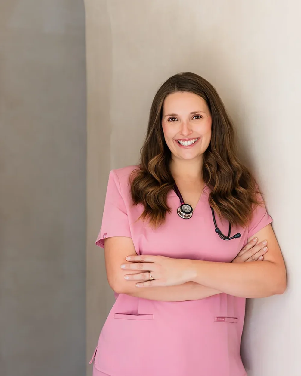 Courtney Garland in pink scrubs with a stethoscope, leaning against a pale wall